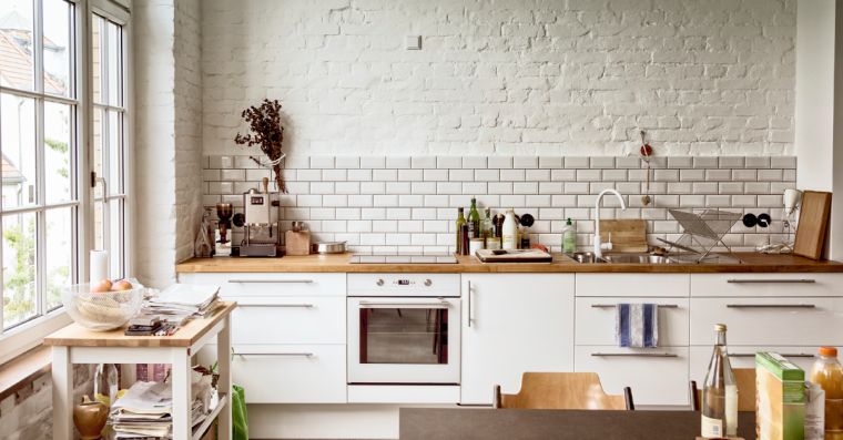 balta virtuvė su mediniais stalviršiais, pramonine apdaila-plytų siena